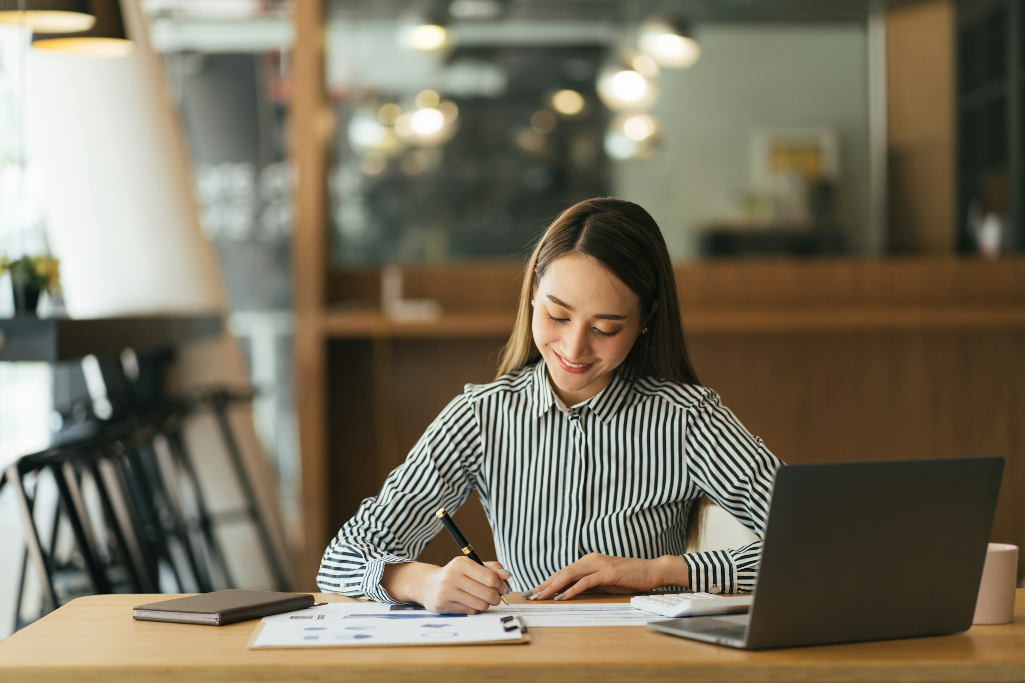 Pensive female administrative assistant checking report on laptop reading information and noting dat
